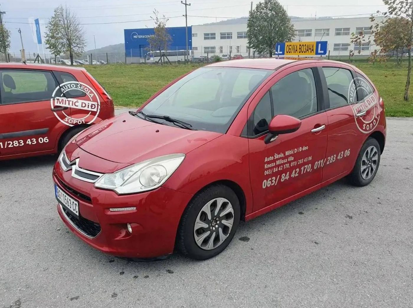 Crveni automobil auto škole Mitić D i Đ sa oznakom L, natpisom Obuka vozača i telefonima na vratima